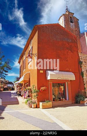 Roussillon, Francia - Ottobre 9. 2019: Vista sulla piazza del borgo antico su colorata casa di pietra naturale ocra e la chiesa medievale campanile contro Foto Stock