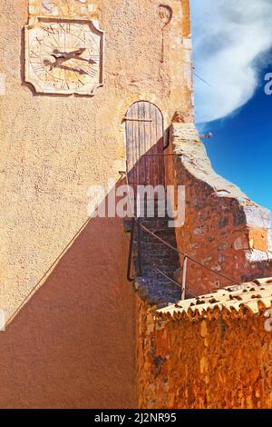 Vista sulla torre muraria in pietra naturale ocra fortezza con orologio, ripide scale strette per l'antica porta di legno ingresso, cielo blu - Roussillon, Francia Foto Stock