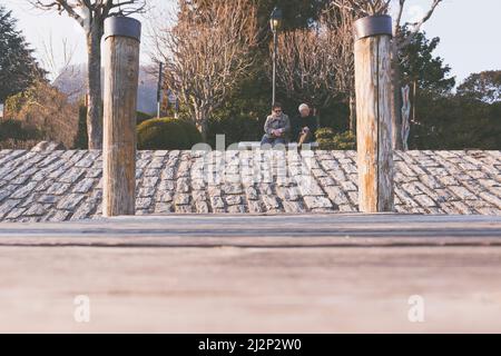 Pella, Italia - 2022.03.26 - una coppia anziana seduta in panchina in un parco pubblico. Vista ad angolo basso. Foto Stock