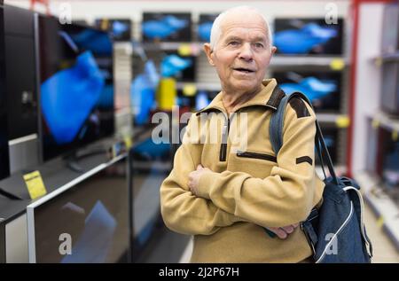 uomo anziano in grigio pensionato in cerca di bancone con moderni televisori digitali in showroom di digital goods store Foto Stock