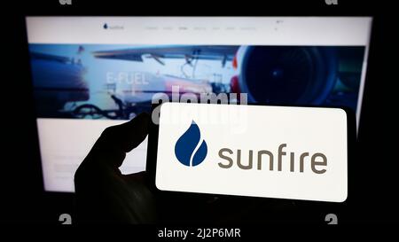 Persona che detiene il cellulare con il logo della società tedesca di energia rinnovabile Sunfire GmbH sullo schermo di fronte alla pagina web. Mettere a fuoco sul display del telefono. Foto Stock