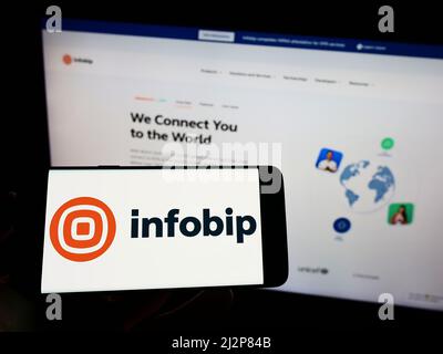 Persona che tiene il cellulare con il logo della società di comunicazioni croata Infobip Ltd. Sullo schermo di fronte al sito web aziendale. Mettere a fuoco sul display del telefono. Foto Stock