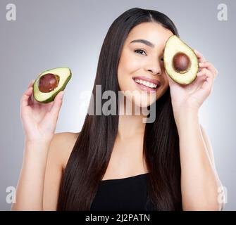 Andare organico era una mossa nella direzione matura per me. Studio ritratto di una giovane donna attraente in posa con un avocado su sfondo grigio. Foto Stock