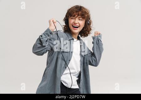 Giovane zenzero gioiosa donna ascoltare musica con cuffie e ballare isolato su sfondo bianco Foto Stock