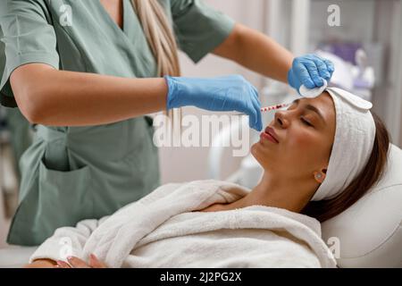 Beautician professionale che fa le iniezioni, riempiendo la faccia femminile con acido ialuronico Foto Stock