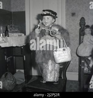 1961, storica, in un abito lucido, top in pelliccia, cappello fantasia, gioielli e borsa a spalla, una giovane ragazza in piedi su una sedia, vestita per il suo compleanno come 'Lady Docker', Stockport, Manchester, Inghilterra, Regno Unito. Nel dopoguerra britannico, Lady Docker - nato Norah Royce Turner in un appartamento sopra un macellaio a Derby - era una 'personalità', una socialite. Attraverso il matrimonio, in particolare il suo terzo matrimonio con Sir Bernard Docker, presidente della Daimler e direttore della Midland Bank, ha condotto per il tempo una vita colorata e stravagante, ma non ha mai dimenticato le sue umili radici della classe operaia. Foto Stock