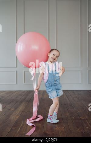 Una ragazza con un grande palloncino rosa che gioca in interni. Ragazzo allegro che tiene un pallone Foto Stock