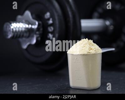 polvere di proteina del siero di latte in paletta con dumbbell su sfondo nero Foto Stock