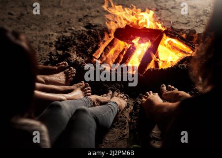 Incollaggio con il falò. Scatto corto di un gruppo di amici irriconoscibili seduti attorno ad un falò sulla spiaggia di notte. Foto Stock