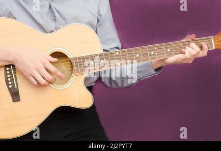 Giovane che suona la chitarra su sfondo viola scuro con spazio copia. Foto Stock