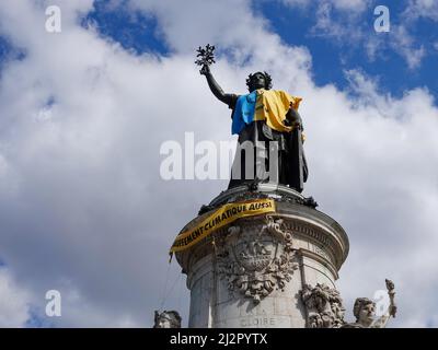 Monumento alla Repubblica, adornato con un gilet giallo e blu nei colori della bandiera Ucraina, insieme con il simbolo della ribellione di estinzione, movimento internazionale sociale ambientale, in protesta della guerra in Ucraina e l'uso eccessivo di petrolio e il suo ruolo nella distruzione del clima. 2 aprile 2022, Parigi, Francia Foto Stock