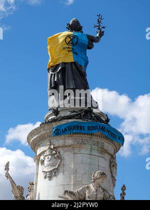 Monumento alla Repubblica, adornato con un gilet giallo e blu nei colori della bandiera Ucraina, insieme con il simbolo della ribellione di estinzione, movimento internazionale sociale ambientale, in protesta della guerra in Ucraina e l'uso eccessivo di petrolio e il suo ruolo nella distruzione del clima. 2 aprile 2022, Parigi, Francia Foto Stock