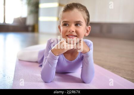 Bambina che indossa un abito viola . Ragazza sorridente carina che si trova sul pavimento su un tappeto sportivo Foto Stock