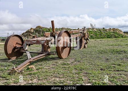 Aratro arrugginito vecchio sul bordo di un campo agricolo Foto Stock