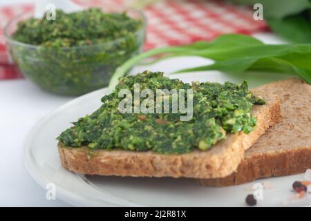 Pesto di porro selvatico con olio d'oliva e noci su sfondo bianco. Spalmare e foglie di ramson fresco. Un sano vegano a colazione. Foto Stock