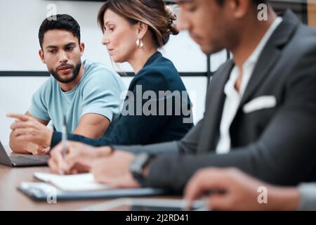 Scambio di idee e informazioni. Scatto corto di due giovani uomini d'affari che parlano nella sala riunioni durante una riunione con i loro colleghi. Foto Stock