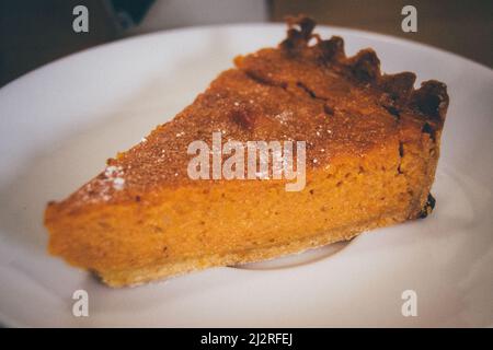 Una fetta di torta di zucca fatta in casa con una crosta di pasta sfoglia e cosparso di zucchero si siede su un piatto di ceramica bianca. Foto Stock