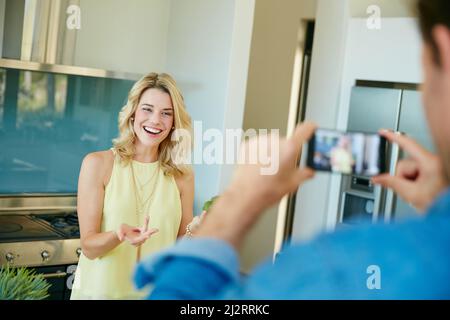 Registrando i loro propri video domestici di cottura. Scatto di un marito che scatta foto di sua moglie che prepara un pasto sano a casa. Foto Stock