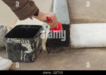 Vernice nera sulla spazzola. Pennello per la verniciatura della superficie. Uso di vernice impermeabile all'esterno. Dipingere il bordo. Il contrassegno della zona pedonale. Foto Stock