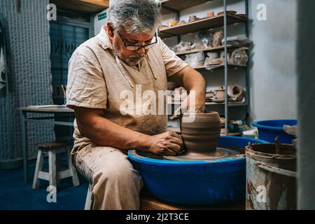 Un vasaio esperto che lavora l'argilla con le mani sulla ruota di un vasaio, modellandola mentre gira. Concetto di artigianato fatto a mano. Foto Stock