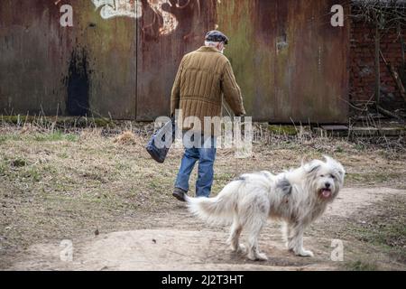 Un uomo anziano cammina per la strada con un cane. In pensione in Russia. Passeggiata di un vecchio uomo in abiti vecchi. Foto Stock