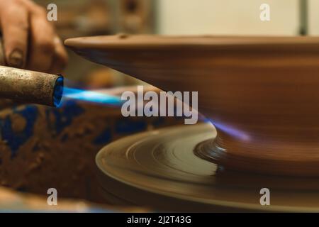 Primo piano di una torcia con fuoco che asciuga il pezzo formato sulla ruota del vasaio. Concetto di artigianale. Foto Stock