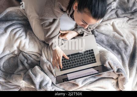 Una donna che lavora su un computer portatile mentre si trova a letto, vista dall'alto. Foto Stock