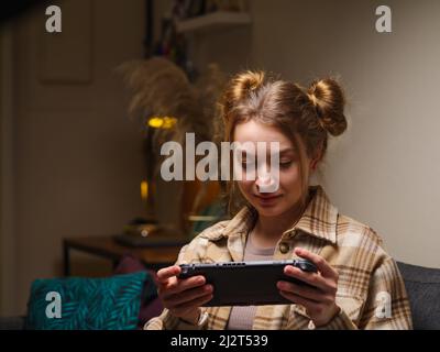 Una ragazza carina con una console di gioco portatile gioca un videogioco. Giochi mobili, tecnologie moderne, cyberspazio, realtà virtuale, intrattenimento, comunicazione Foto Stock