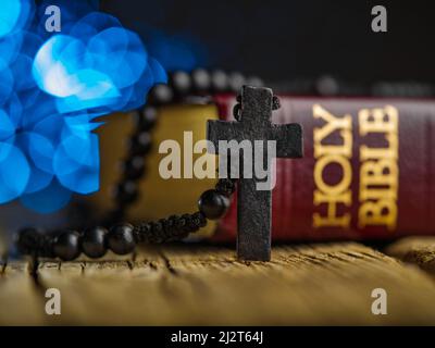 Su un tavolo di legno si trova un libro rosso - la Sacra Bibbia e un rosario con una croce su sfondo blu scuro. Gesù Cristo, sacra Scrittura, religione, catodo Foto Stock