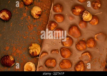 Cioccolato con nocciole e polvere di cacao su sfondo di ardesia. Dessert al cioccolato con noci. Bar di cioccolato su sfondo scuro. Dessert e dolci Foto Stock