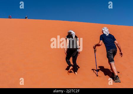 Due persone che arrampicano sulla duna di sabbia rossa, Wadi Rum, Giordania, Asia. Foto Stock
