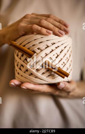 Primo piano le belle mani femminili tengono il rotolo del hank del filato beige del nastro e degli aghi del crochet di legno Foto Stock