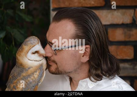 Uomo con gufo a casa. Animali domestici insoliti e rapporti umani di amicizia animale. Uccello selvatico a portata di mano guanto tenerezza e amore. Foto Stock