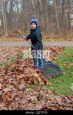 La giovane ragazza rastrella lascia nel suo cortile in un freddo giorno di caduta Foto Stock
