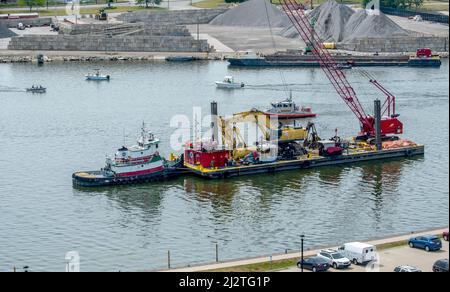 Giugno 19 2021 St Joseph MI USA; Una barca tira una chiatta da costruzione carica di attrezzature pesanti lungo il fiume saint Joseph Foto Stock