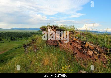 Formazioni di pietra arenaria stratificate sulla cima di un'alta collina che domina l'infinita steppa estiva. Catena montuosa Chests, Khakassia, Siberia, Russia. Foto Stock