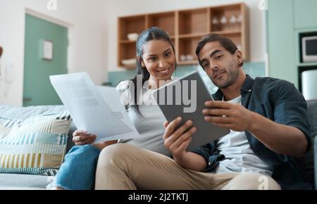 Lavorare per il nostro futuro un passo alla volta. Scatto di una giovane coppia che fa la documentazione mentre usa un tablet digitale a casa. Foto Stock