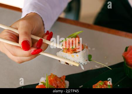 Sushi Roll su un piatto nero con le mani donna che tiene chopsticks, cibo giapponese Foto Stock