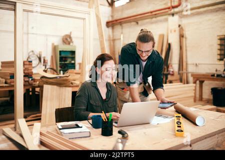 Weve ha avuto un sacco di lavoro da fare oggi. Scatto ritagliato di due giovani carpentieri utilizzando un notebook e un tablet digitale che lavorano insieme all'interno del loro laboratorio. Foto Stock