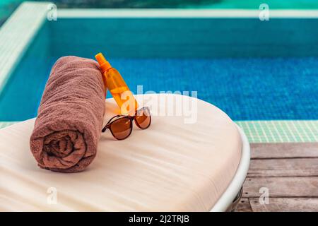 Suntan vacanza hotel piscina sfondo con accessori di viaggio per abbronzarsi su lettini vacanze nella destinazione dei Caraibi. Olio abbronzante, asciugamano Foto Stock