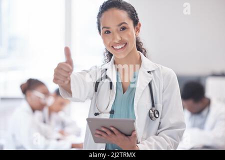 Approvo. Ritratto corto di una giovane ragazza attraente medico dando i pollici in su e usando un tablet mentre si levano in piedi nella sala del consiglio con lei Foto Stock