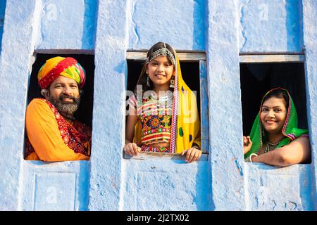 Felice indiano tradizionale famiglia che indossa tradizionale vestito di rajasthan colorato guardando fuori dalla finestra., rurale india. Foto Stock