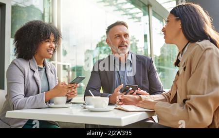 Quando avete capito questo. Foto di un gruppo di colleghi che hanno brainstorming idee in un bar mentre utilizzano i loro smartphone. Foto Stock