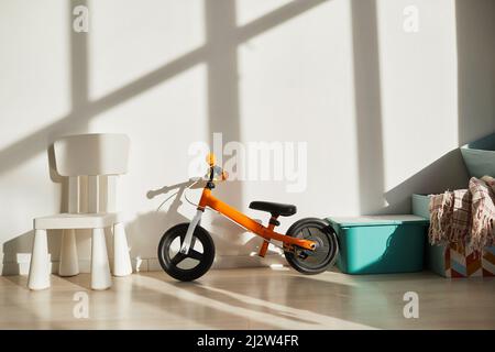 Immagine di sfondo minimale della moto vibrante per bambini con bilanciamento contro la parete bianca nella stanza dei bambini illuminata dalla luce del sole, spazio copia Foto Stock