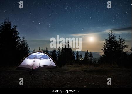 Tenda illuminata posto sul bordo di sentiero di pietra sulla collina di montagna. Incredibile bellezza del paesaggio serale. Chiaro di luna, nuvole basse su sfondo di cielo stellato. Colline di montagna in lontananza. Foto Stock