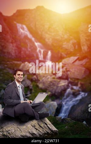 Uomo d'affari che lavora sul suo laptop in alta montagna accanto ad una cascata al tramonto, immagine concettuale della libertà Foto Stock