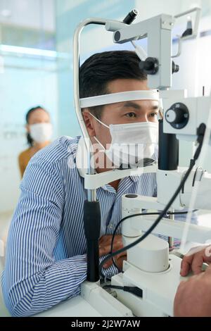 Uomo asiatico che viene testato per il glaucoma con attrezzature moderne in ufficio di optometristo Foto Stock