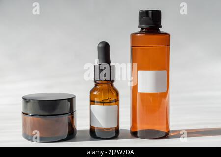 Bottiglie in vetro cosmetico con crema, toner e maschera facciale su sfondo grigio con ombre dure. Il concetto di bellezza naturale cosmetici Foto Stock