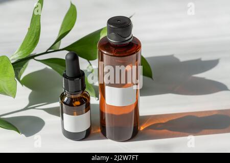 Set di cosmetici per l'igiene personale sul tavolo. Beauty olio viso con estratti naturali e toner pelle con ombre dure e foglie di rusco Foto Stock