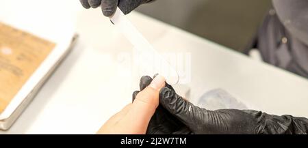 Primo piano delle mani caucasiche di un manicurista professionale stanno archiviando le unghie di una giovane donna. Giovane donna caucasica che riceve una manicure da un estetista con una lima del chiodo in un salone del chiodo Foto Stock